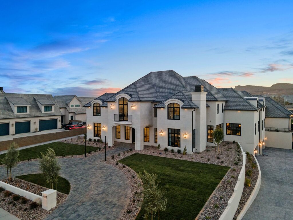 Custom luxury home by RL Wyman Design + Create in St. George, UT, featuring modern architecture, expansive driveway, landscaped yard, and elegant exterior lighting at dusk.