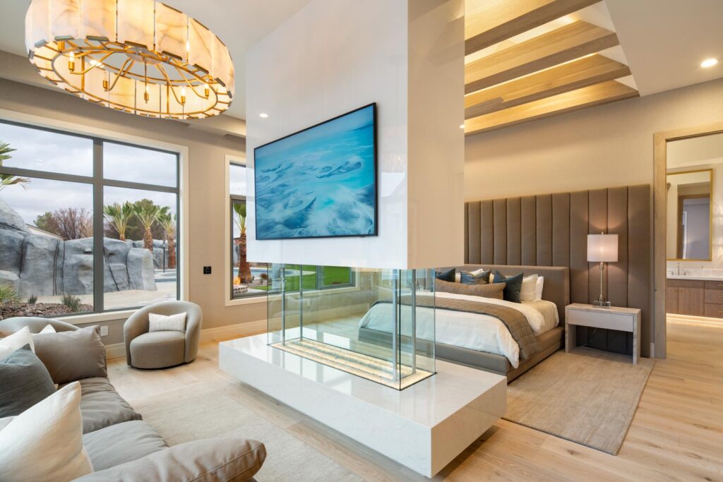 Luxury master bedroom featuring modern design elements, a central glass fireplace, large windows with views of palm trees, and contemporary furnishings, highlighting RL Wyman's custom home craftsmanship in Mesquite, Nevada.