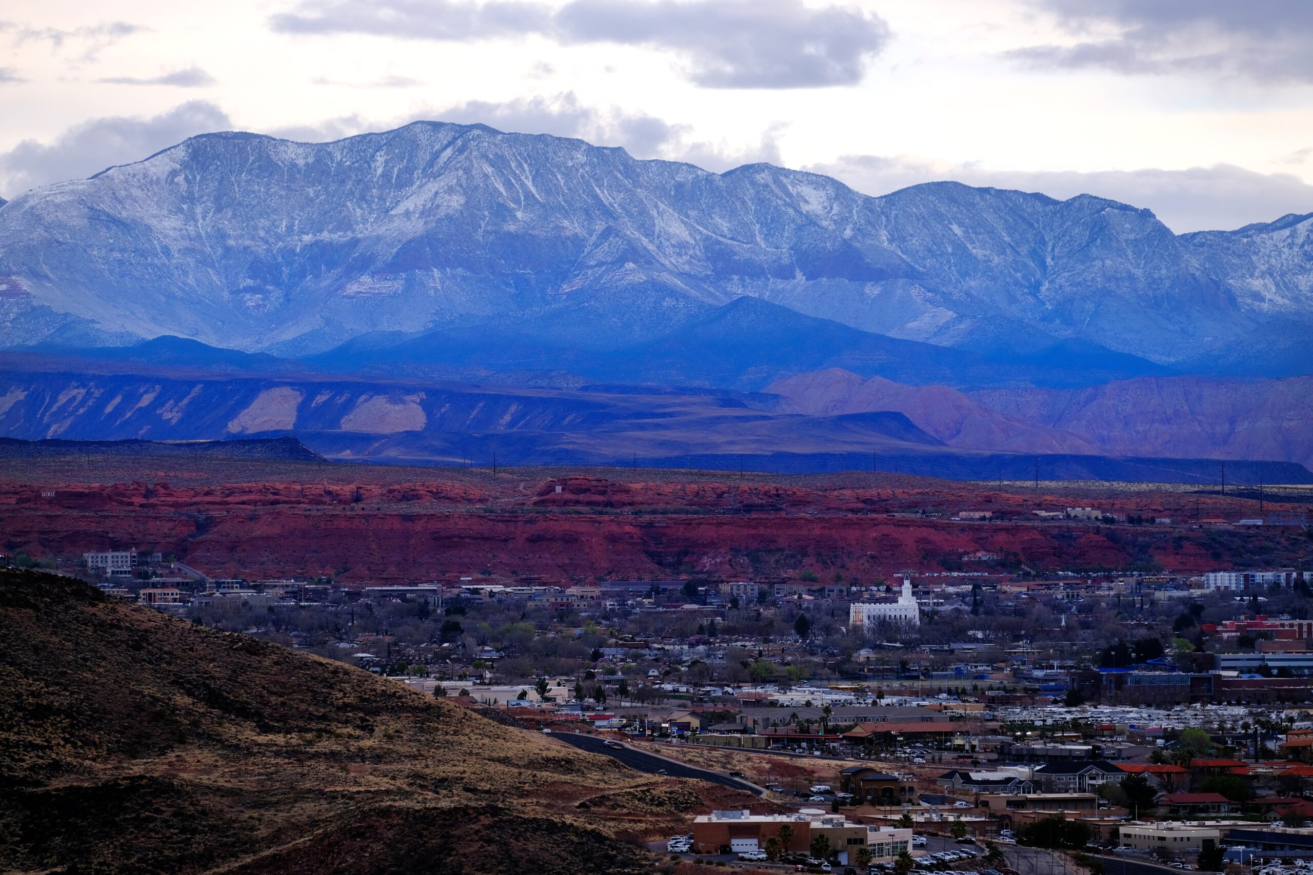 Stunning view of St. George, Utah, featuring red rock formations, snow-capped mountains, and a vibrant community landscape, illustrating the ideal location for custom home building by RL Wyman Design + Create.