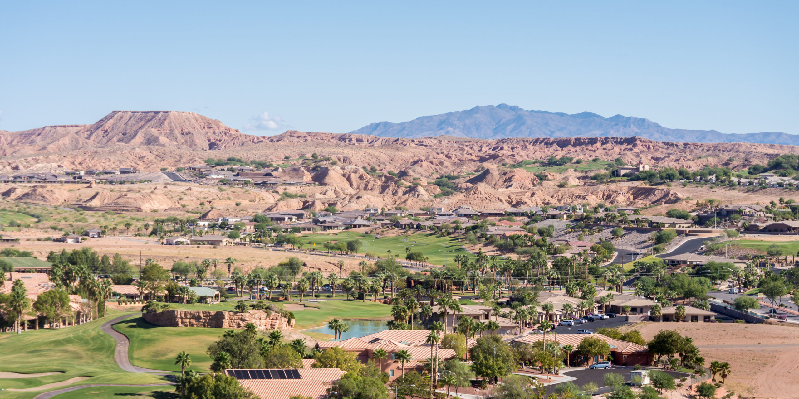 Desert landscape in Mesquite, Nevada, showcasing custom homes, lush golf courses, and mountainous terrain under a clear blue sky.